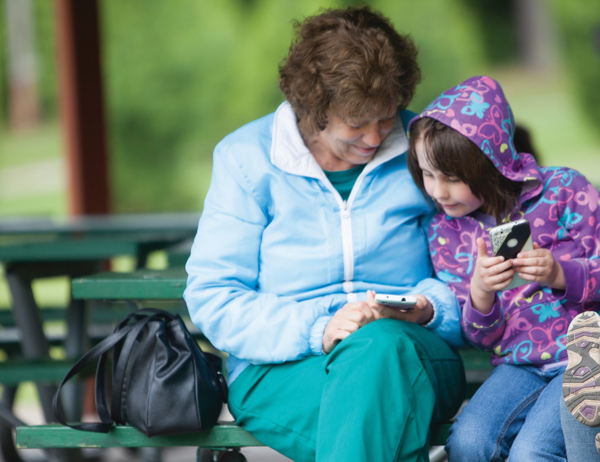 Young girl leans in close to older woman, looking at a phone.