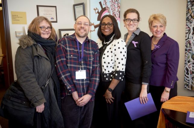 A group of people pose after an advocacy meeting with a legislator. Two of them wear purple ribbons to show their support for the epilepsy community.