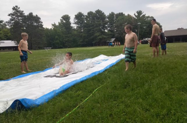 Campers in bathing suits take turns on a slip-and-slide at camp oz