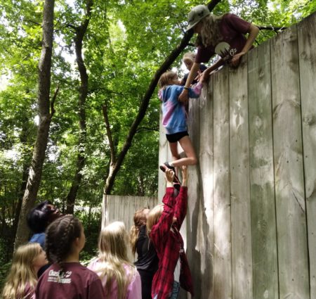 Campers help each other scale a wood wall in a team-building activity
