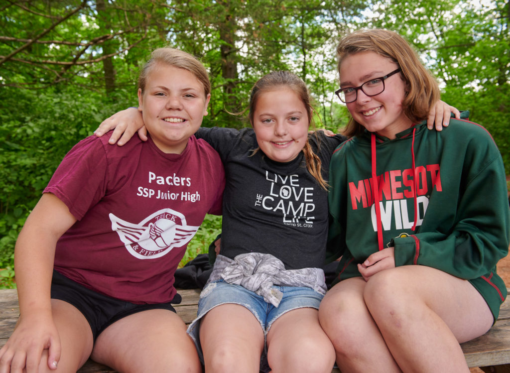 Three girl campers smiling with trees in the background