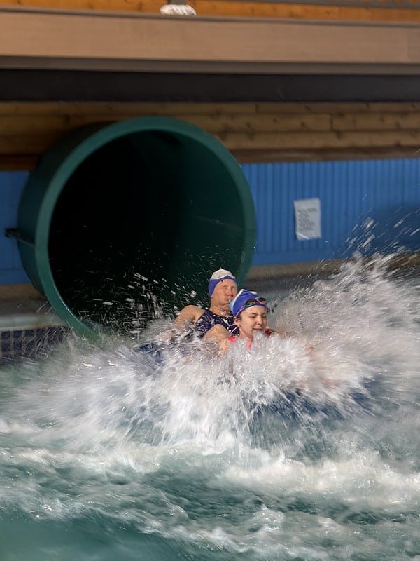 Attendees with swim caps and goggles splashing as they come out of the waterslide at the waterpark