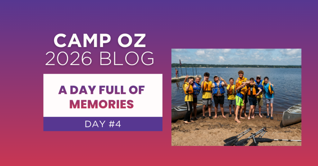 Camp Oz 2026 Blog – A Day Full of Memories, Day #4” featuring a group of campers wearing life jackets standing together on a lakeshore next to canoes and paddles, with a dock and calm water in the background under a partly cloudy sky